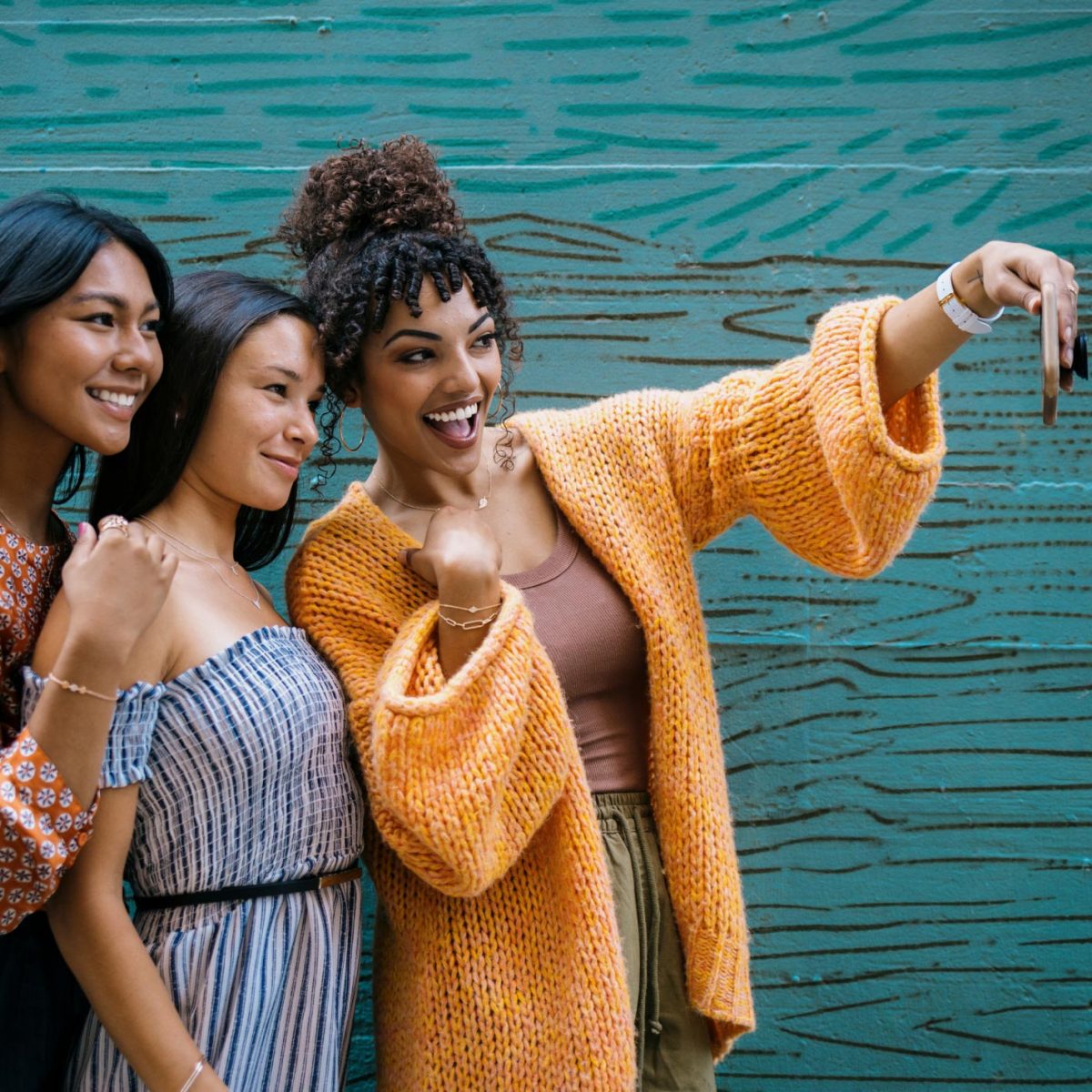 Three women taking a selfie in front of a green murial wall