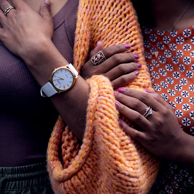 two women's arms interlocked with one wearing a watch and one wearing rings